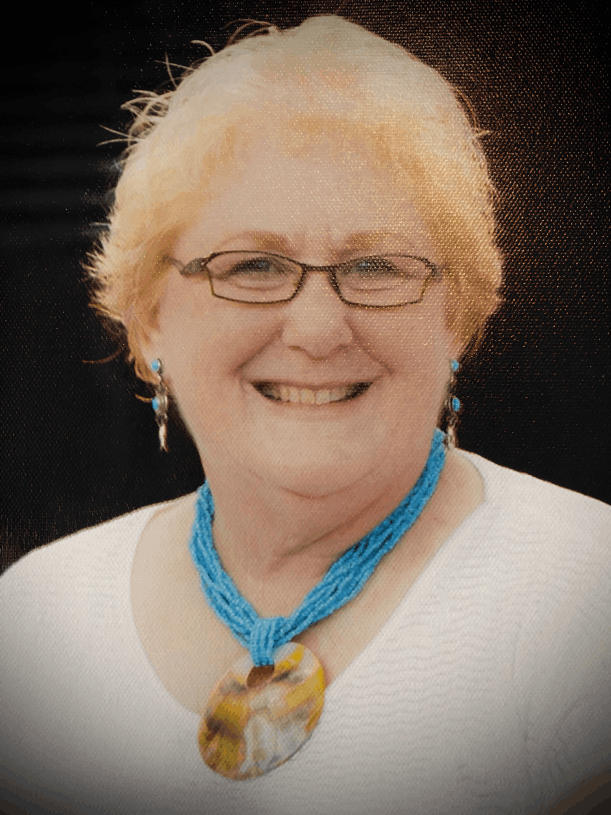 Female caucasian with strawberry blonde hair wearing a white blouse, a turquoise pendant, and matching earrings, glasses, and a smile.